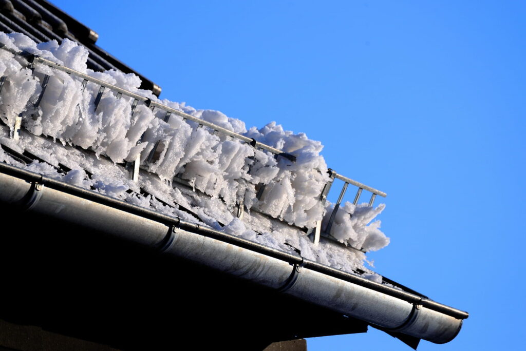 Homeowner inspecting roof edge for ice dams after a snowfall