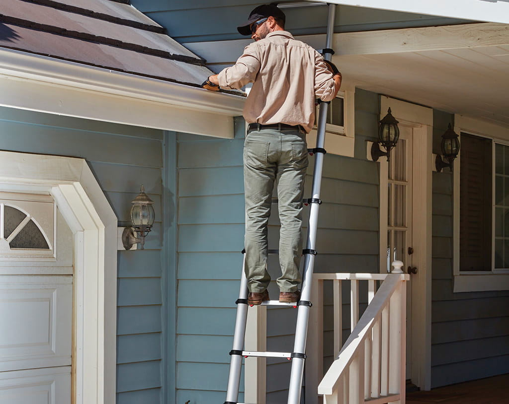 Homeowner cleaning gutters in spring to prevent water damage
